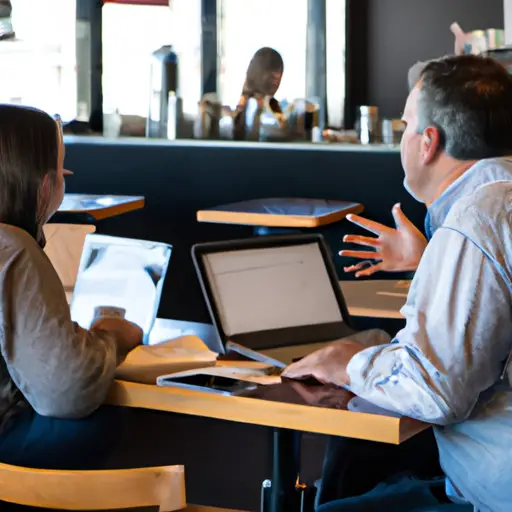 An image showing two coworkers sitting at separate tables in a coffee shop, engrossed in their own activities, subtly implying their intentional disconnection