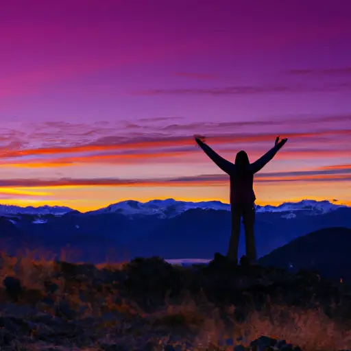 An image of a person standing on a mountain peak, arms open wide, as the vibrant sunrise paints the sky with hues of pink and orange