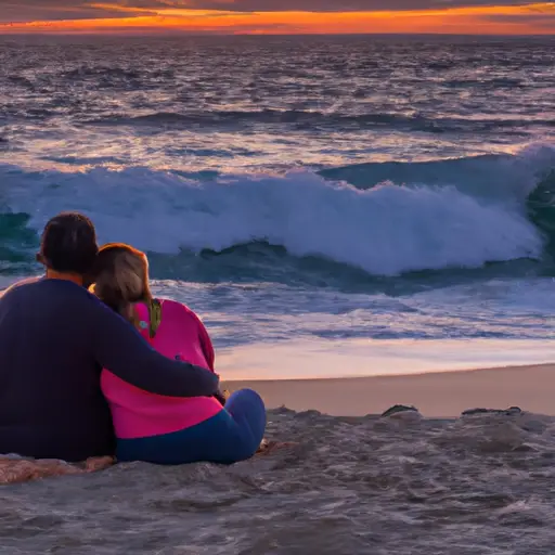 An image of a young couple sitting on a sandy beach at sunset, their arms wrapped around each other
