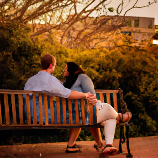 Capture an image of a couple sitting on a bench in a park at sunset, their eyes locked in a tender gaze, as he holds her hand gently, displaying remorse and sincerity, while she cautiously contemplates forgiveness